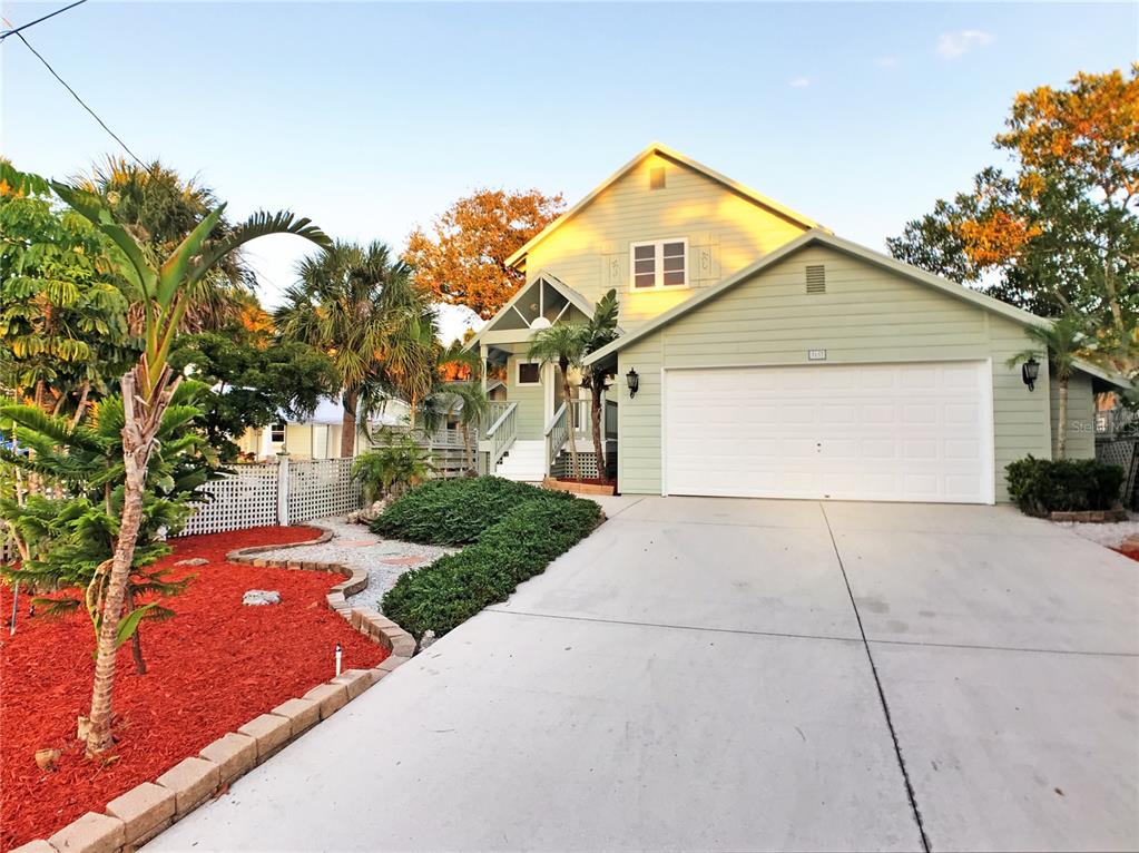 A light green two-story house features a white garage door and a landscaped front yard — 5157 SANDY BEACH AVENUE, SARASOTA, FL