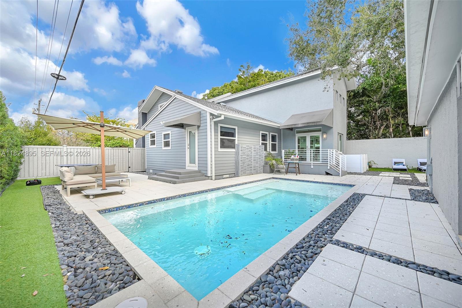 A backyard features a rectangular swimming pool, light-colored patio pavers, and a two-story gray house — 150 NE 50 # A, Miami FL 33137, MIAMI, FL