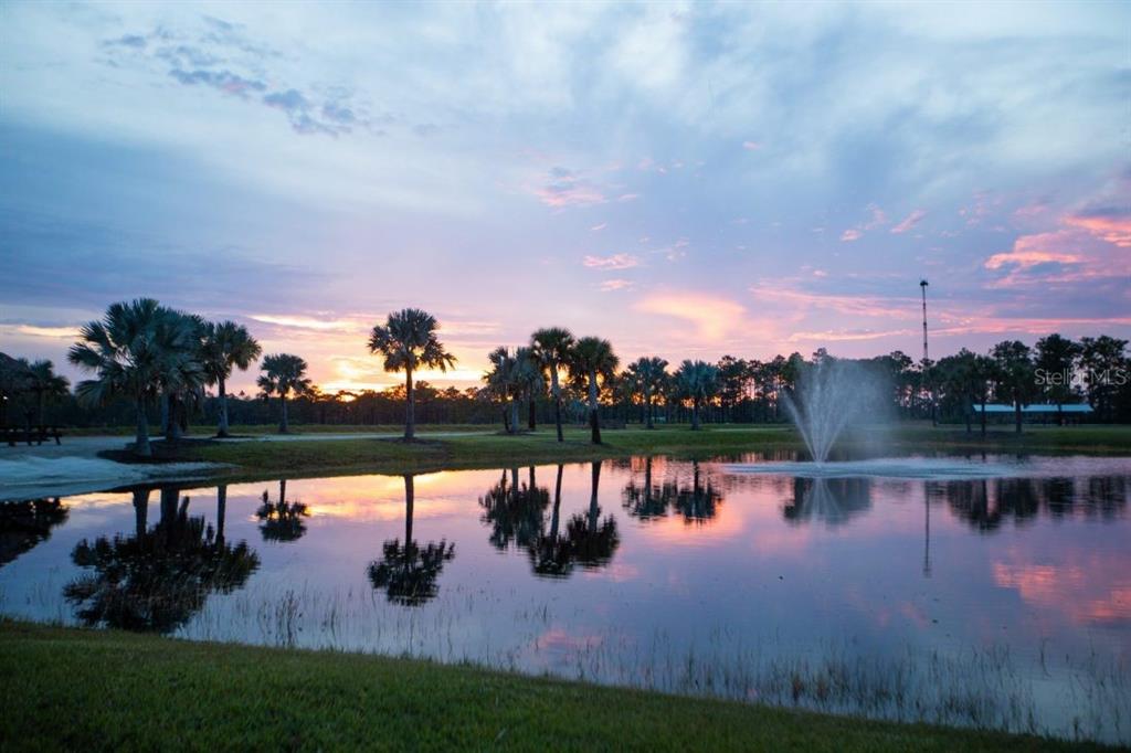 A pond with a fountain reflects palm trees and a sunset sky in a grassy field — 124 RHETT BOULEVARD E, LAKE WALES, FL