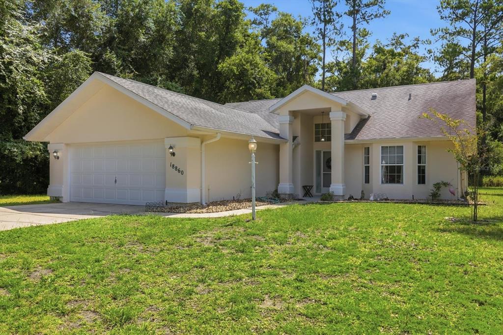 A single-story house with a two-car garage, beige stucco siding, and a covered front entryway — 18860 SW 99TH STREET, DUNNELLON, FL