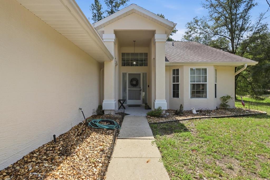 A concrete walkway leads to the covered front entrance of a beige stucco house — 18860 SW 99TH STREET, DUNNELLON, FL