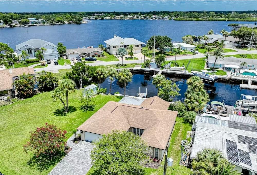 An aerial view shows a waterfront house with a brown roof, lawn, and boat dock — 8116 BRIGHTON DRIVE, PORT RICHEY, FL
