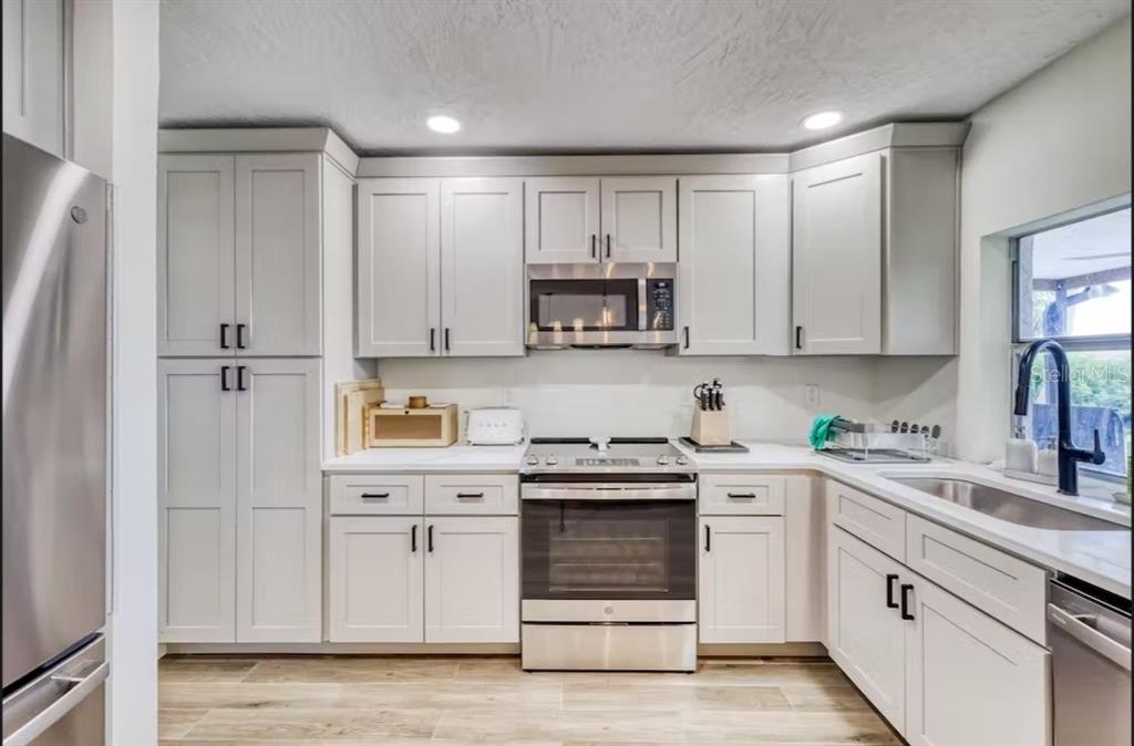 A kitchen with light gray cabinets, stainless steel appliances, white countertops, and wood-look flooring — 8116 BRIGHTON DRIVE, PORT RICHEY, FL