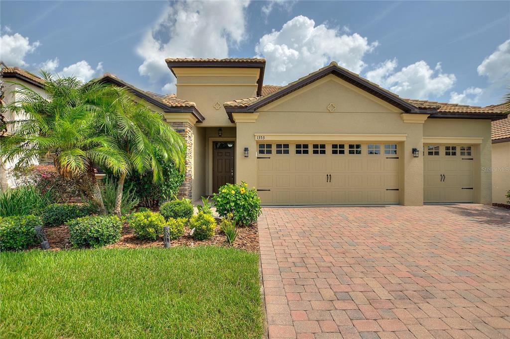 A tan single-story house with a tiled roof, a three-car garage, and a paved driveway — 1353 PALMETTO DUNES ST, DAVENPORT, FL