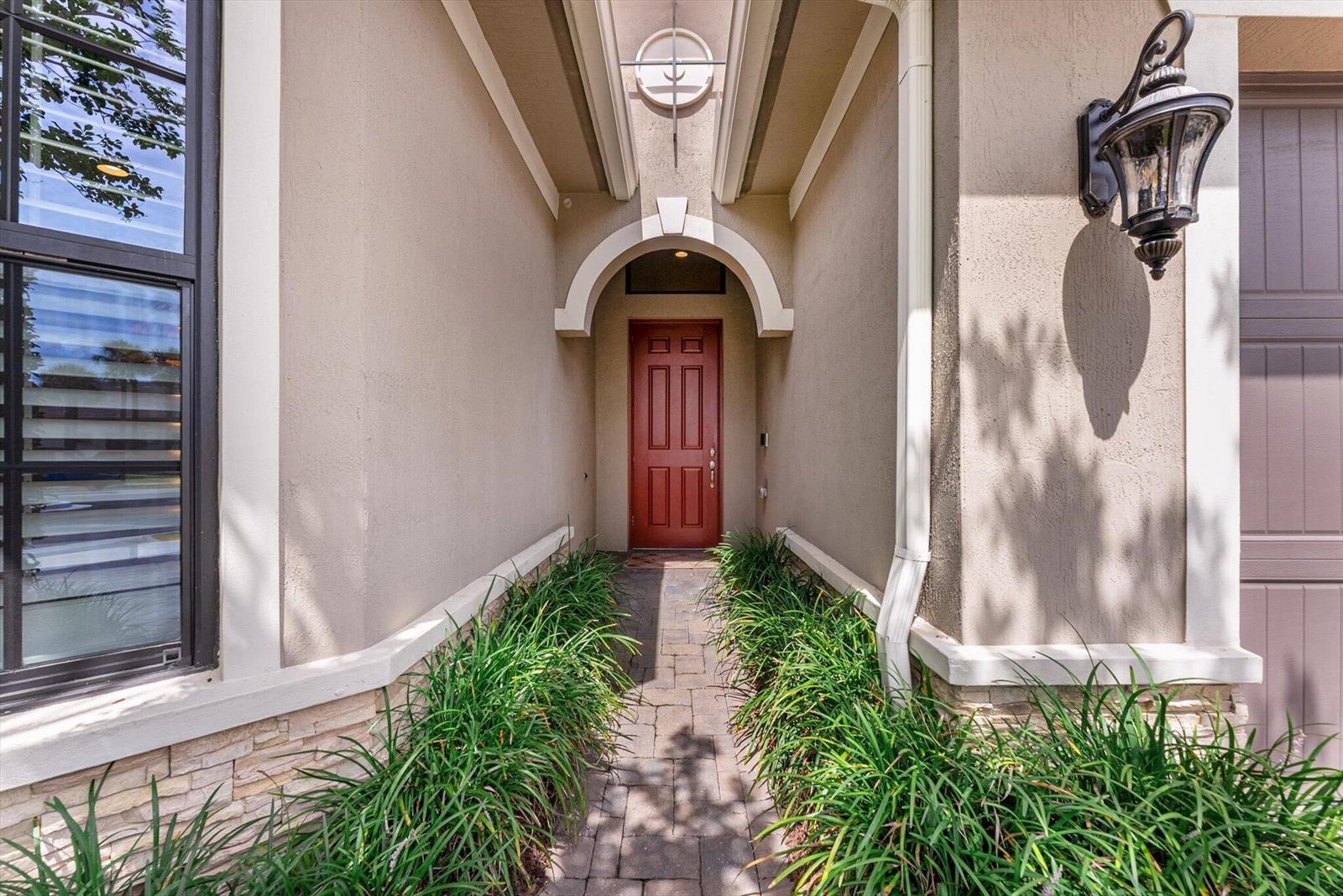 A red front door is accessed by a stone walkway lined with green plants — 9505 Kalmar Circle W, Parkland FL 33076, PARKLAND, FL