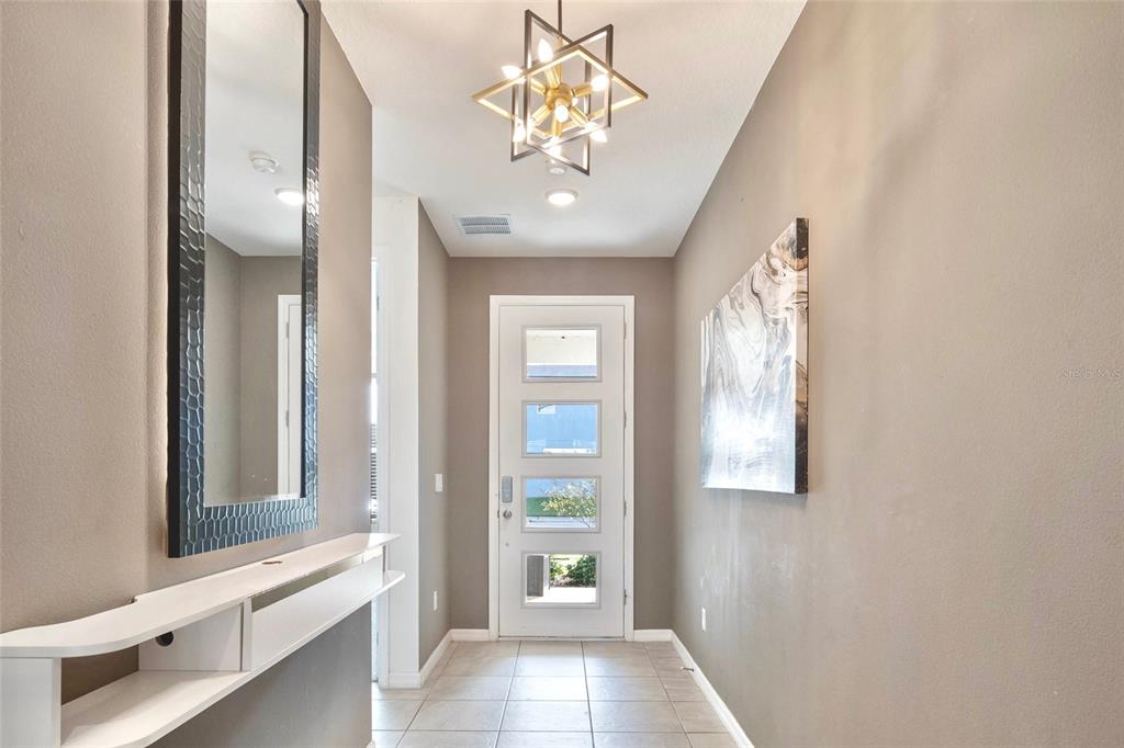 A modern entryway features a white door with glass panels, a chandelier, and a mirror — 1594 MERMAID COVE WAY, KISSIMMEE, FL
