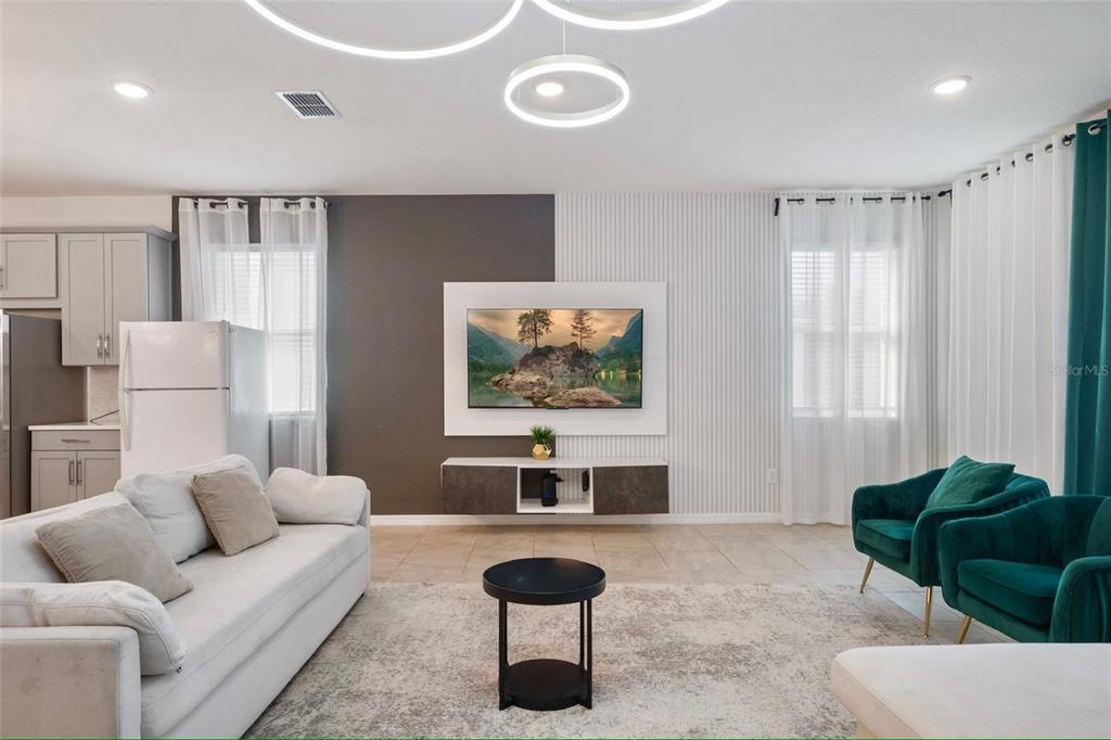 A living room features a two-tone accent wall, a floating media console, and teal armchairs — 1594 MERMAID COVE WAY, KISSIMMEE, FL
