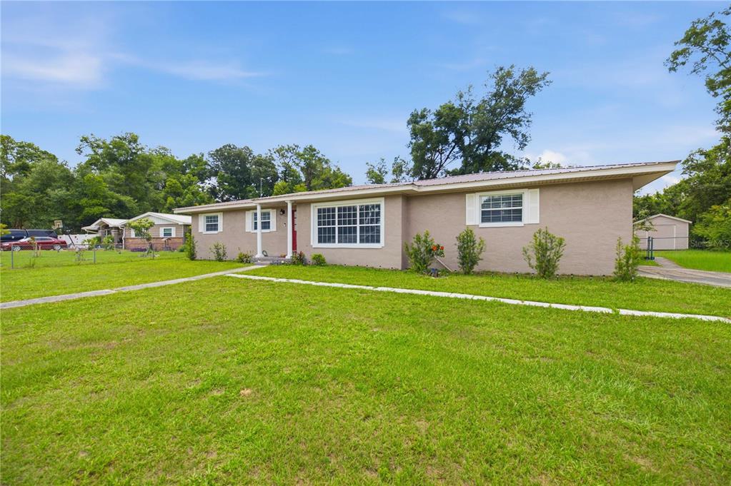 A single-story house with a tan stucco exterior, a metal roof, and a large front lawn — 4218 SE 14TH PLACE, OCALA, FL