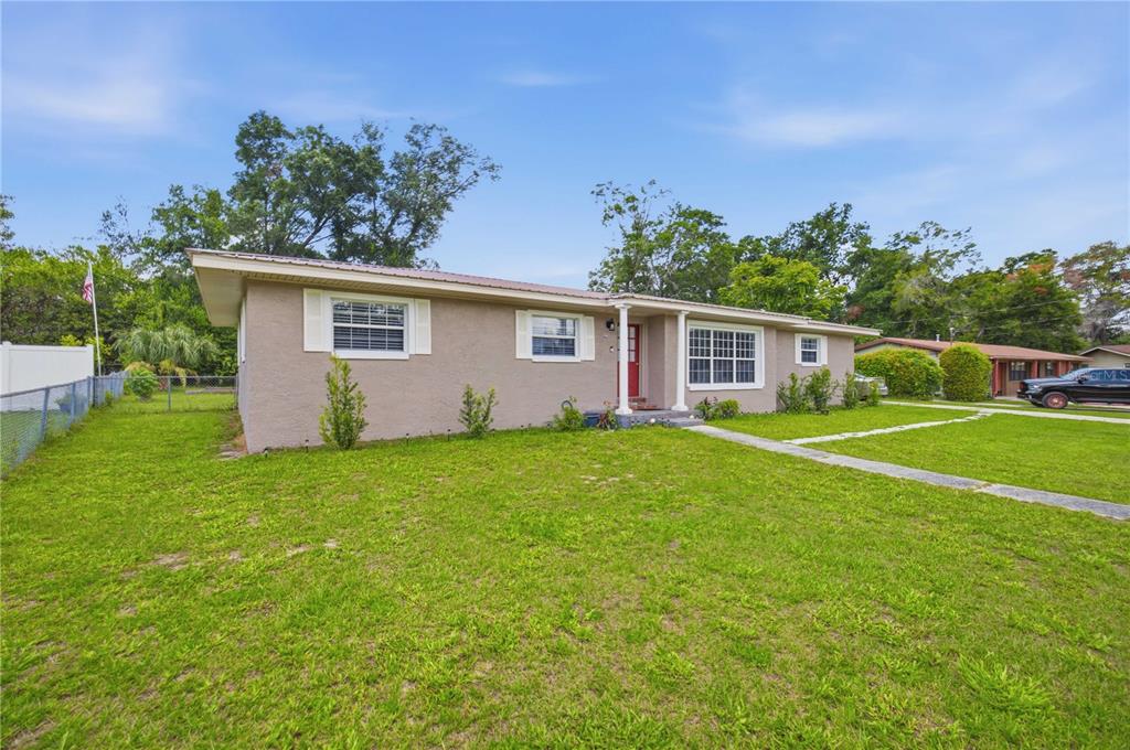 A single-story house with a tan stucco exterior, a red front door, and a metal roof — 4218 SE 14TH PLACE, OCALA, FL