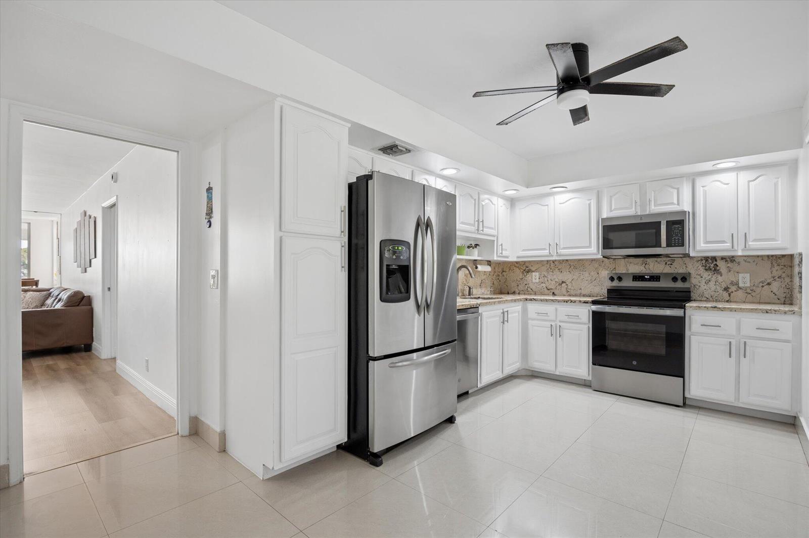 A kitchen with white cabinets, stainless steel appliances, and granite countertops features a ceiling fan — 804 Cypress Grove Lane # 308, Pompano Beach FL 33069, POMPANO BEACH, FL