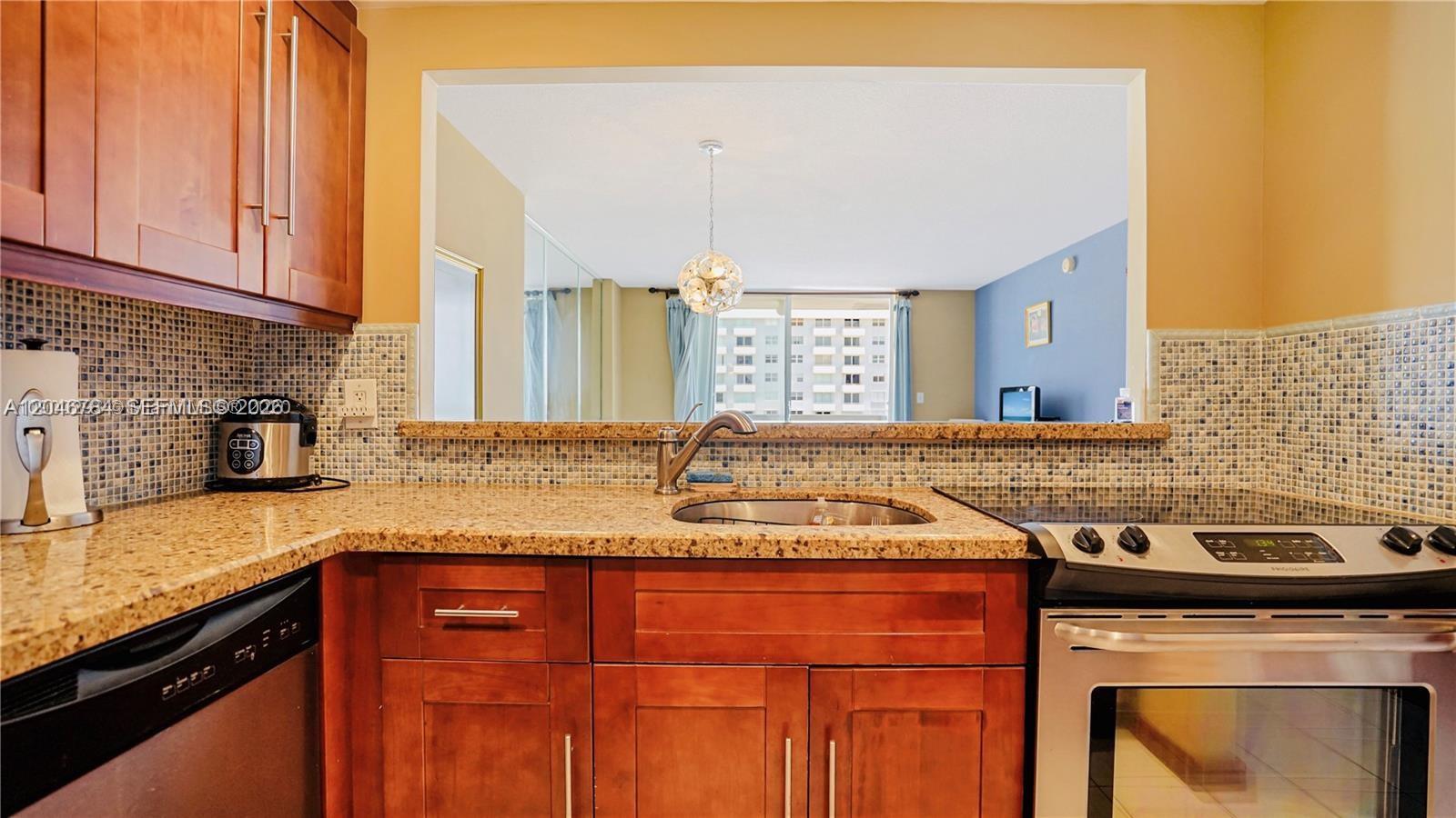 A kitchen features wood cabinets, granite countertops, a tiled backsplash, and a pass-through window — 401 Ocean Dr # 722, Miami Beach FL 33139, MIAMI BEACH, FL