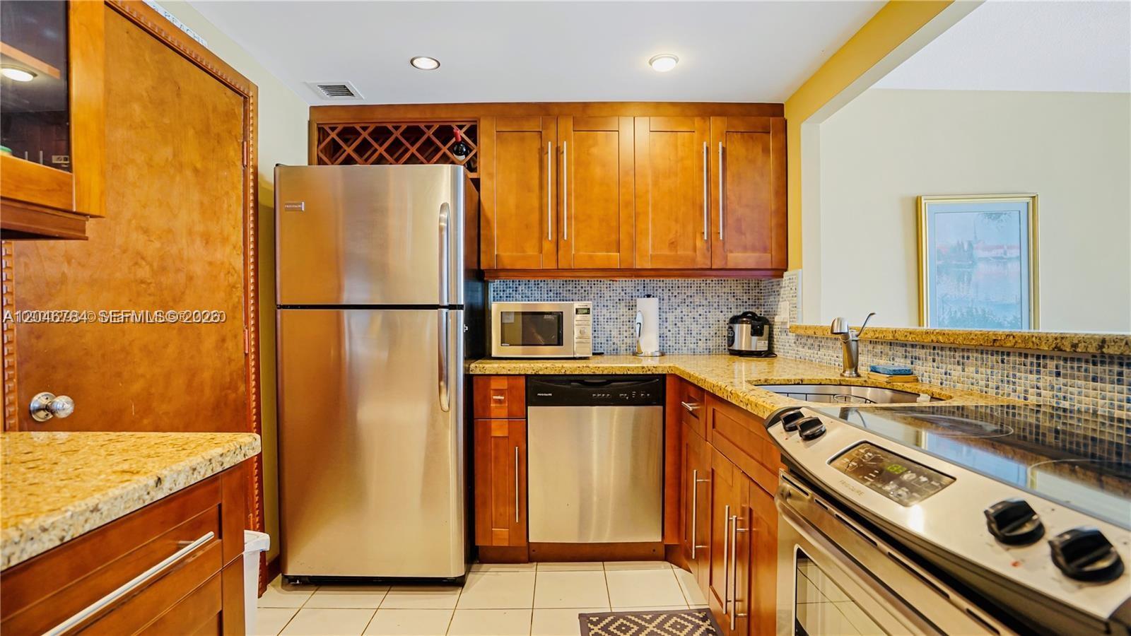 A kitchen features wood cabinets, stainless steel appliances, and a blue mosaic tile backsplash — 401 Ocean Dr # 722, Miami Beach FL 33139, MIAMI BEACH, FL