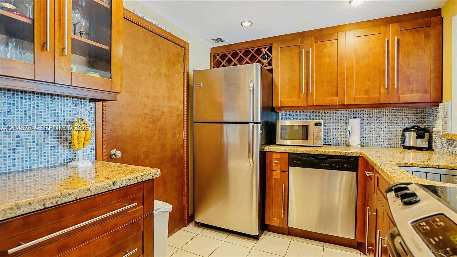 A kitchen features wood cabinets, granite countertops, stainless steel appliances, and a blue mosaic backsplash — 401 Ocean Dr # 722, Miami Beach FL 33139, MIAMI BEACH, FL
