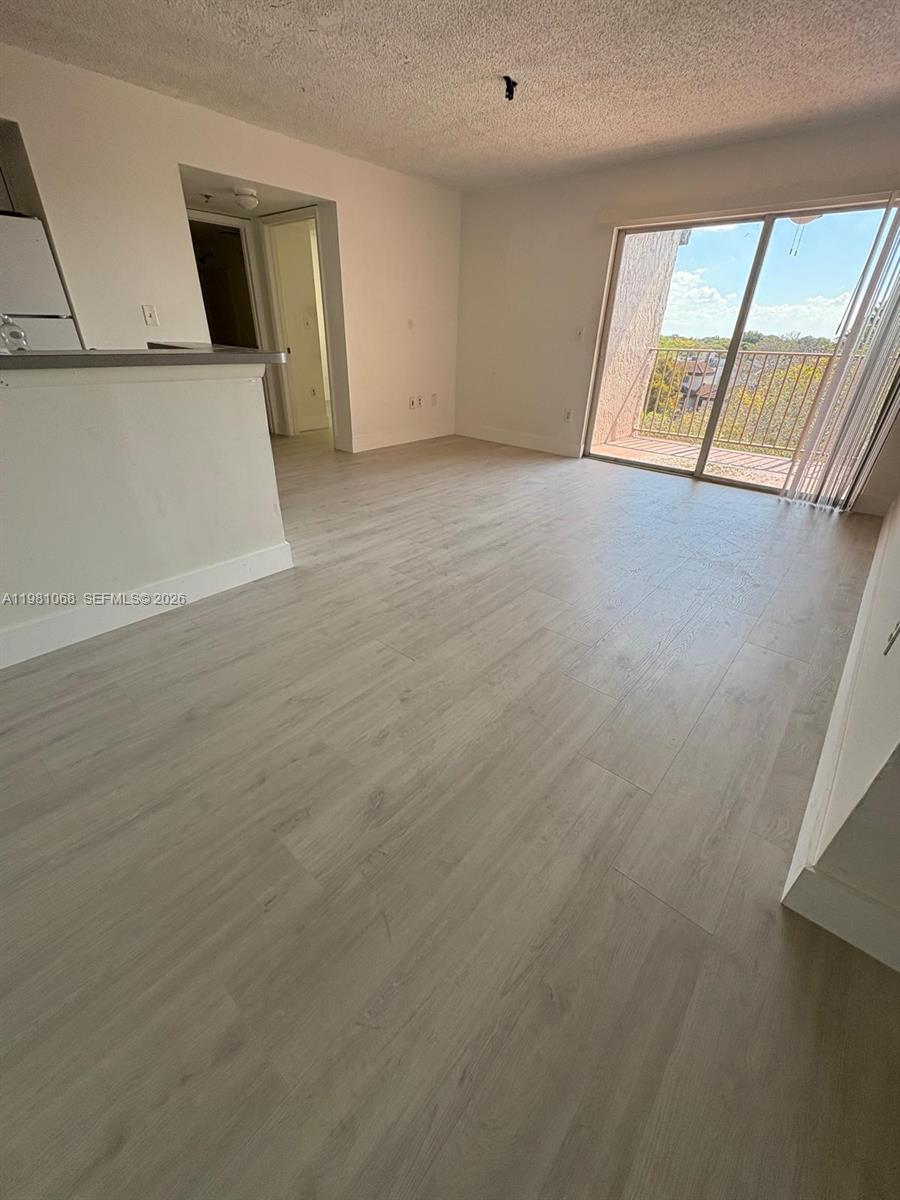 An empty living area features light-colored wood-look flooring and a sliding glass door to a balcony — 15231 SW 80th St # 615, Miami FL 33193, MIAMI, FL