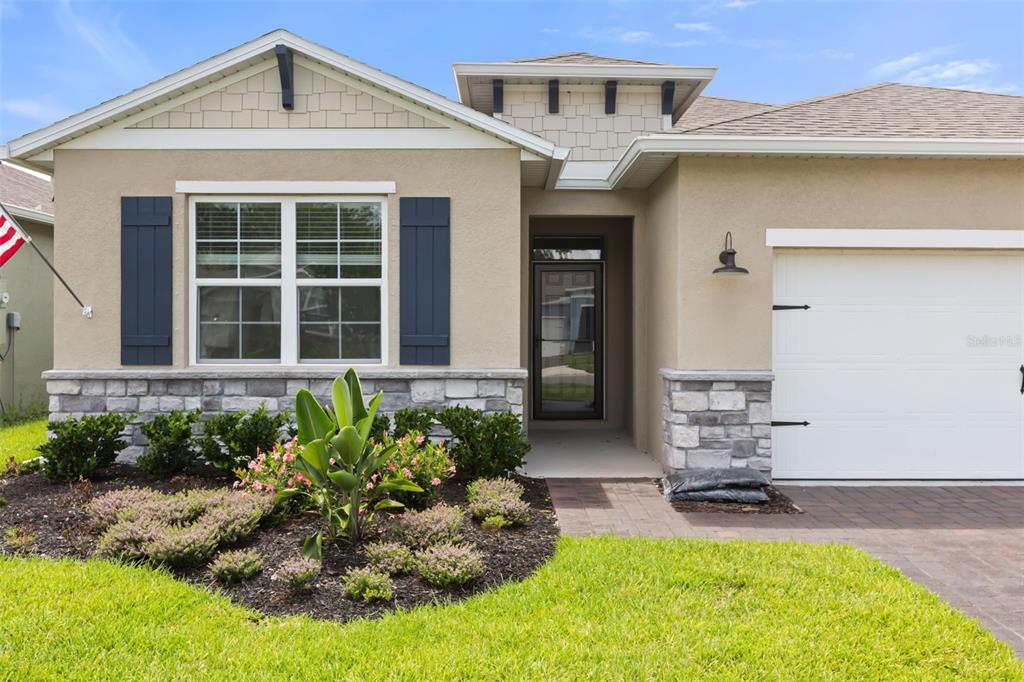 A single-story house with tan stucco, stone veneer, blue shutters, and a paved driveway — 1545 DELPHI WAY, NEW SMYRNA BEACH, FL