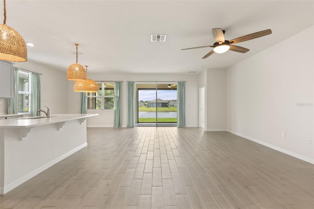 An open-concept kitchen and living area features light wood-look tile flooring and a sliding glass door — 1545 DELPHI WAY, NEW SMYRNA BEACH, FL