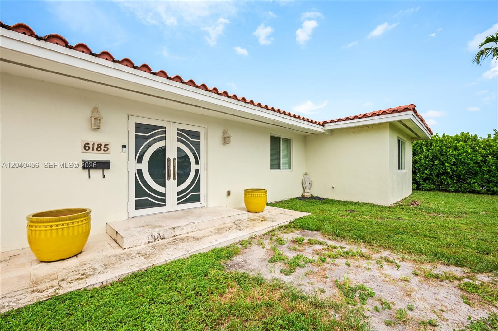 The exterior of a house features a double door entrance, yellow planters, and a tiled roof — 6185 W 10th Ave, Hialeah FL 33012, HIALEAH, FL