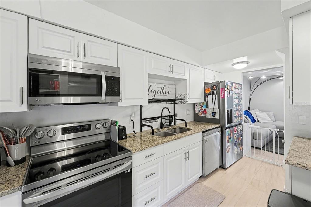 A kitchen features white cabinets, stainless steel appliances, granite countertops, and a wall-mounted spice rack — 1819 CLEARBROOKE DRIVE, CLEARWATER, FL
