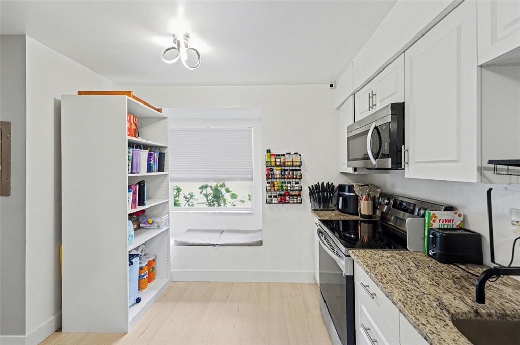 A kitchen features white cabinets, granite countertops, a tall shelving unit, and a window seat — 1819 CLEARBROOKE DRIVE, CLEARWATER, FL
