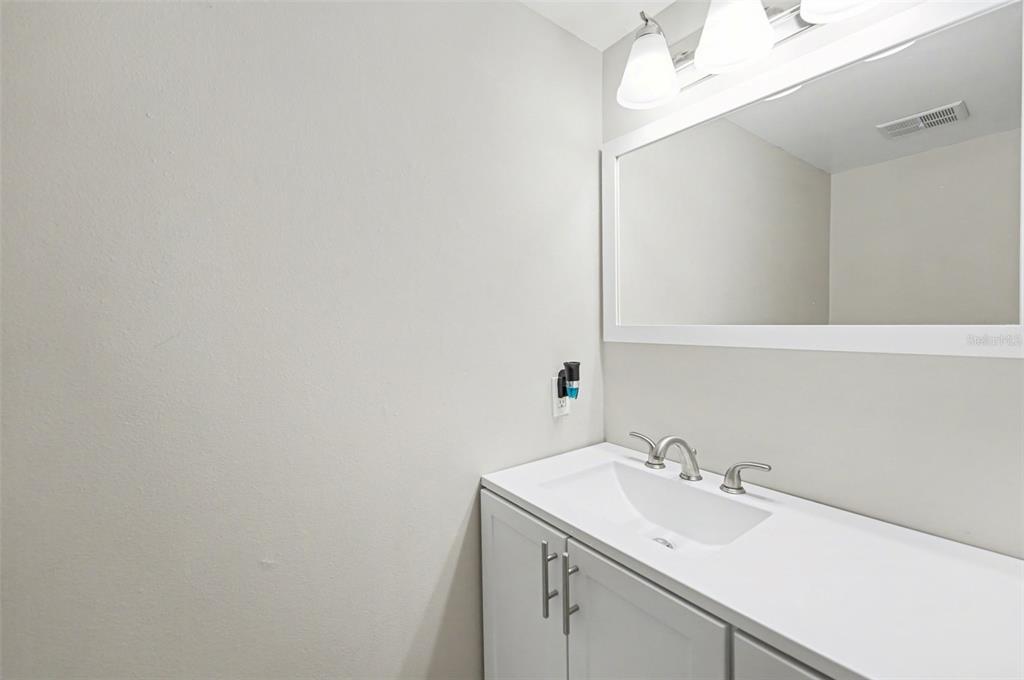 A bathroom features a white vanity with a single sink, a large mirror, and lighting — 1819 CLEARBROOKE DRIVE, CLEARWATER, FL