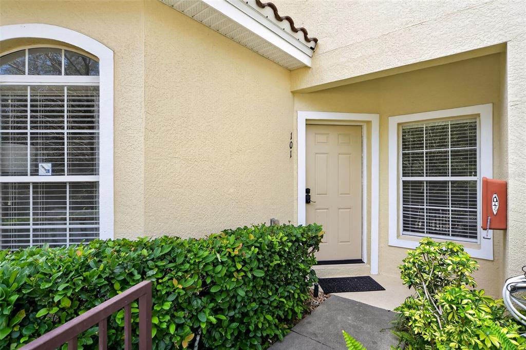 The exterior of a beige home features a front door, two windows, and landscaping — 692 SEABROOK COURT UNIT 101, ALTAMONTE SPRINGS, FL