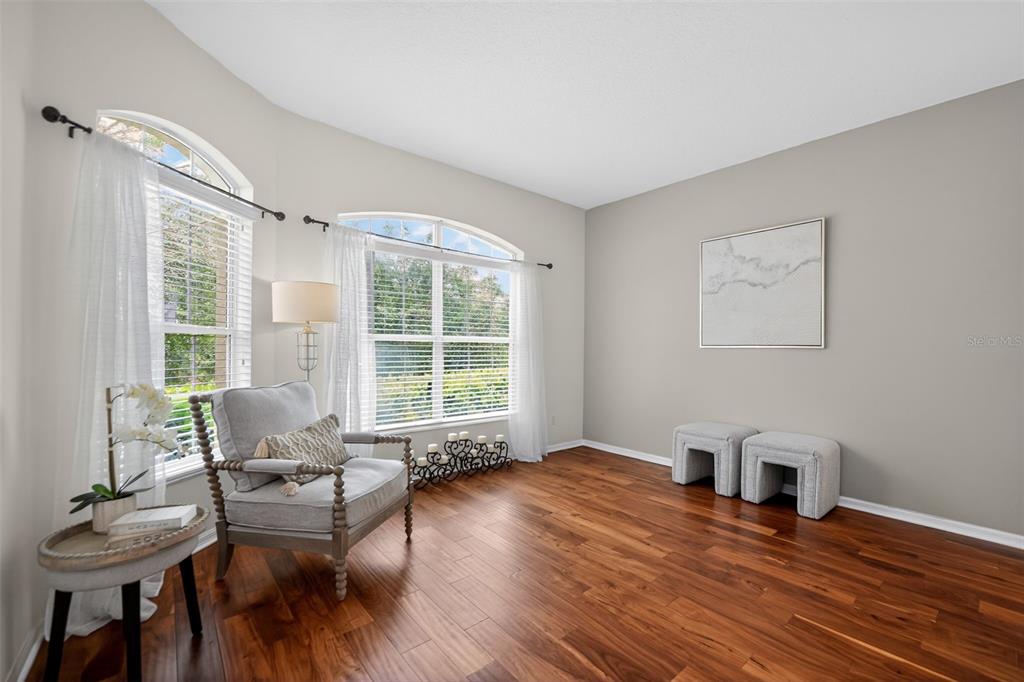 A bright living room features hardwood floors, two arched windows, an armchair, and two ottomans — 692 SEABROOK COURT UNIT 101, ALTAMONTE SPRINGS, FL