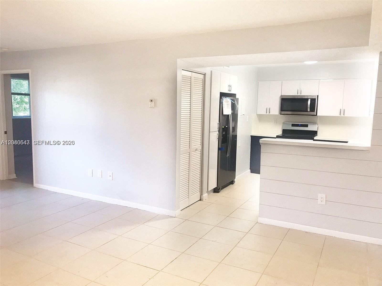 A kitchen with white cabinets and stainless steel appliances opens to a tiled living area — 14971 SW 82nd Ln # 308, Miami FL 33193, MIAMI, FL