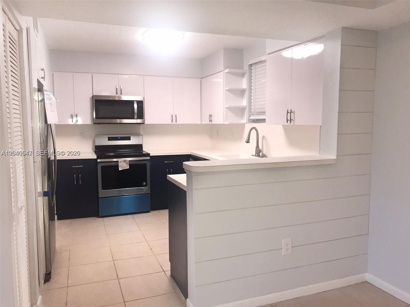 A kitchen features white upper cabinets, dark lower cabinets, stainless steel appliances, and shiplap siding — 14971 SW 82nd Ln # 308, Miami FL 33193, MIAMI, FL