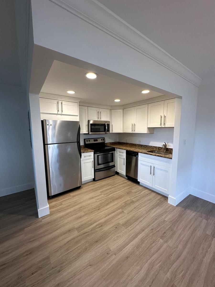 A compact kitchen features white cabinets, stainless steel appliances, and granite countertops — 50 Monaco # B, Delray Beach FL 33446, DELRAY BEACH, FL