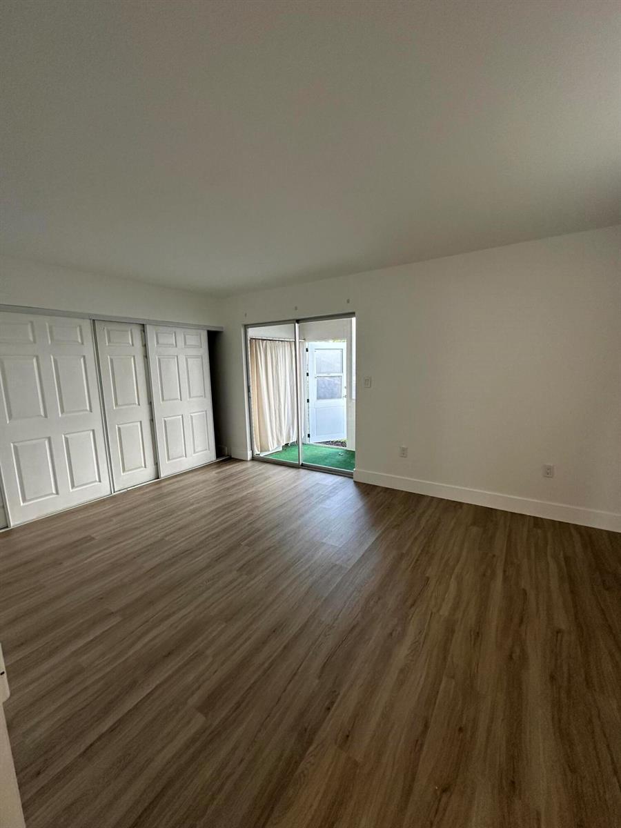 An empty room features light wood-look flooring, white walls, sliding closet doors, and a glass door — 50 Monaco # B, Delray Beach FL 33446, DELRAY BEACH, FL