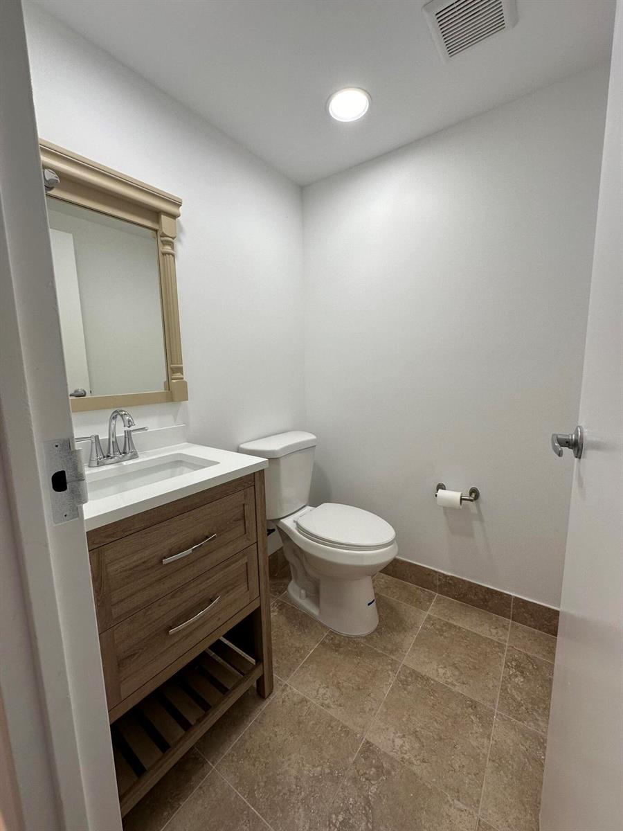 A small bathroom features a wood vanity, a white toilet, and light-colored tile flooring — 50 Monaco # B, Delray Beach FL 33446, DELRAY BEACH, FL