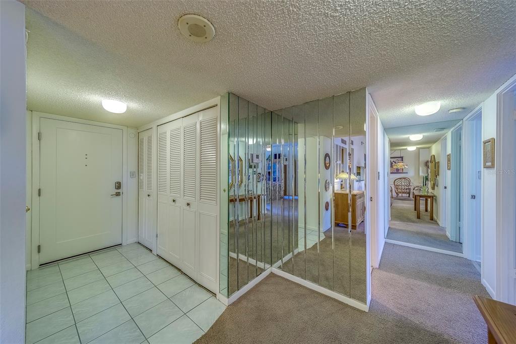 An entryway with white tile floors, louvered closet doors, and a wall of mirrored panels — 400 ISLAND WAY UNIT 104, CLEARWATER BEACH, FL