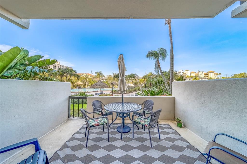 A covered patio features a dining set on a geometric rug overlooking a swimming pool — 400 ISLAND WAY UNIT 104, CLEARWATER BEACH, FL