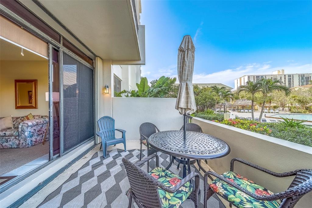 A balcony with a patio table, chairs, and a view of a swimming pool area — 400 ISLAND WAY UNIT 104, CLEARWATER BEACH, FL
