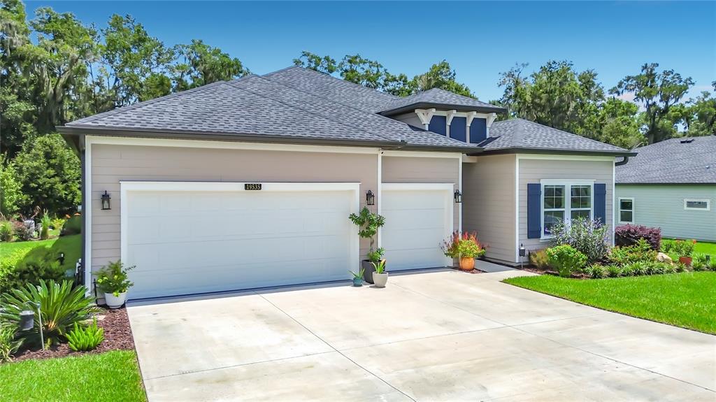 A single-story house with a two-car garage, beige siding, and a dark shingled roof — 19535 SW 77TH LOOP, DUNNELLON, FL