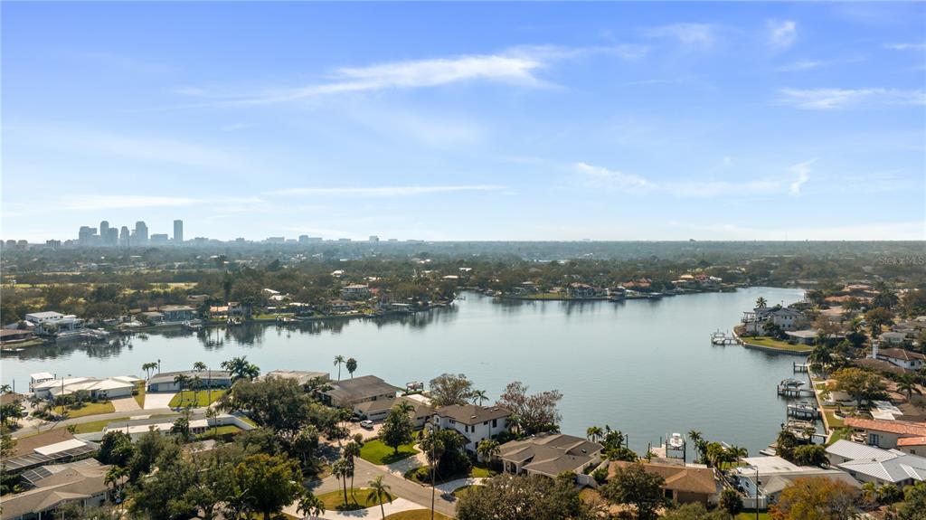 An aerial view shows a residential neighborhood bordering a lake with a distant city skyline — 3598 10TH STREET NE, ST PETERSBURG, FL
