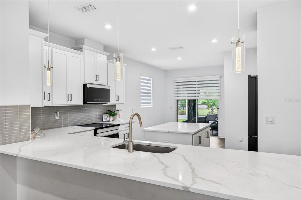 A modern kitchen features white cabinetry, quartz countertops, a central island, and stainless steel appliances — 11404 SUNSAIL AVENUE, ORLANDO, FL
