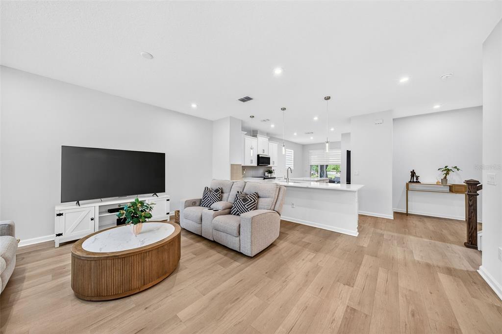 A living room with light wood floors, a television, and an open kitchen island — 11404 SUNSAIL AVENUE, ORLANDO, FL