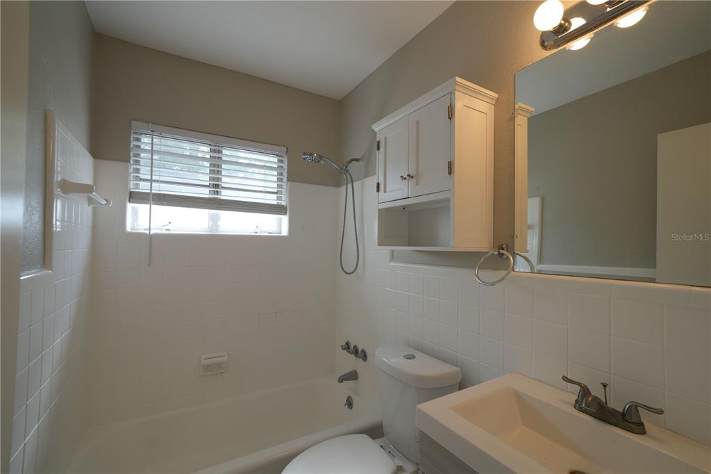 A bathroom features a white tub-shower combination, a toilet, a vanity, and wall-mounted cabinetry — 4517 S CLARK AVENUE, TAMPA, FL