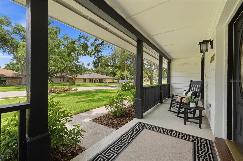 A covered front porch features black railings, a patterned rug, and two wooden rocking chairs — 11007 THERESA ARBOR DRIVE, TAMPA, FL