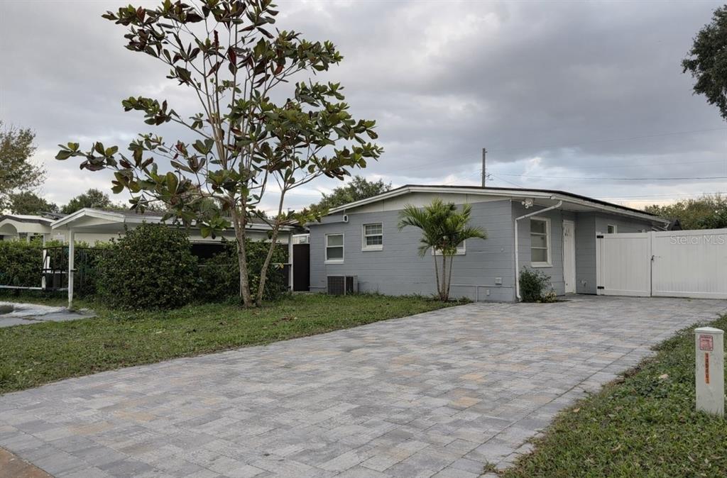 A gray, single-story house features a paved driveway, a small palm tree, and white fencing — 2615 N BEAUMONT AVENUE, KISSIMMEE, FL