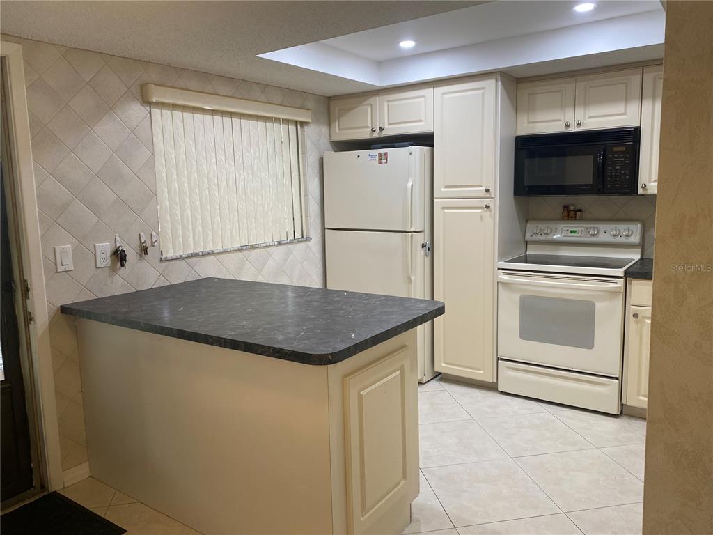 A kitchen features cream-colored cabinets, white appliances, a dark countertop island, and tiled flooring — 2440 WINDING CREEK BOULEVARD UNIT 108, CLEARWATER, FL
