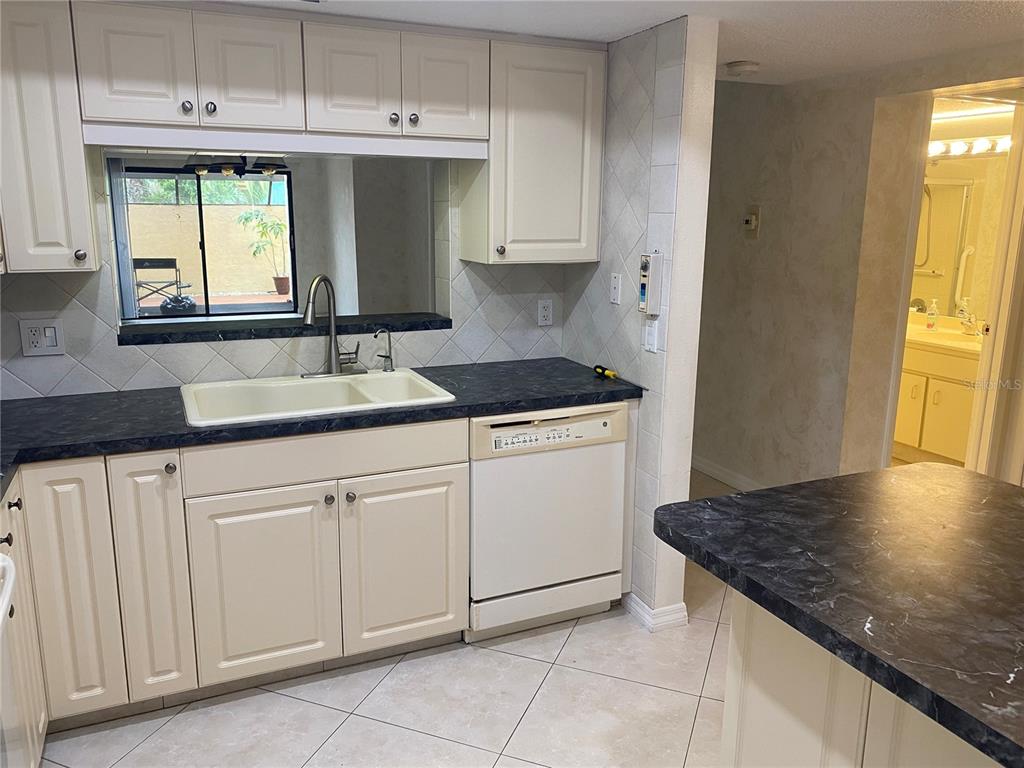 A kitchen features cream cabinets, dark marble-look countertops, a white dishwasher, and a pass-through window — 2440 WINDING CREEK BOULEVARD UNIT 108, CLEARWATER, FL