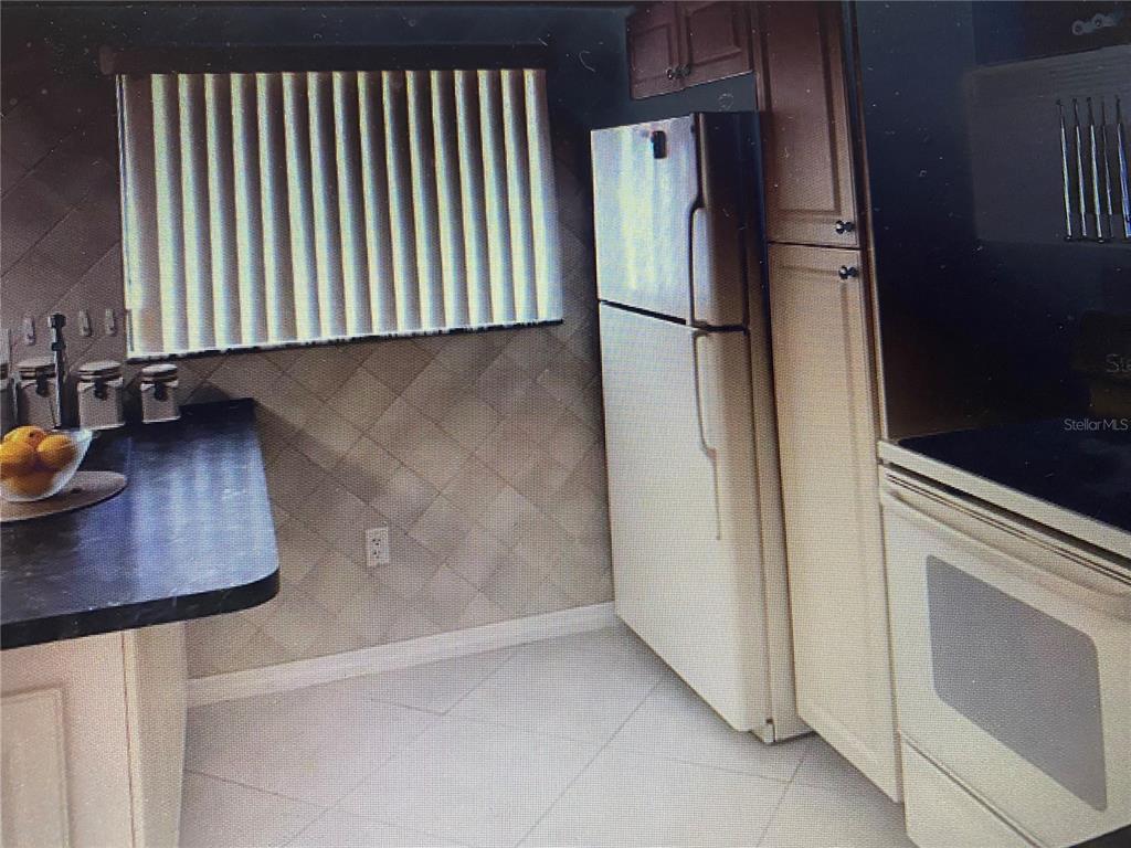 A kitchen features light-colored cabinets, a stainless steel refrigerator, a dark countertop, and tiled walls — 2440 WINDING CREEK BOULEVARD UNIT 108, CLEARWATER, FL