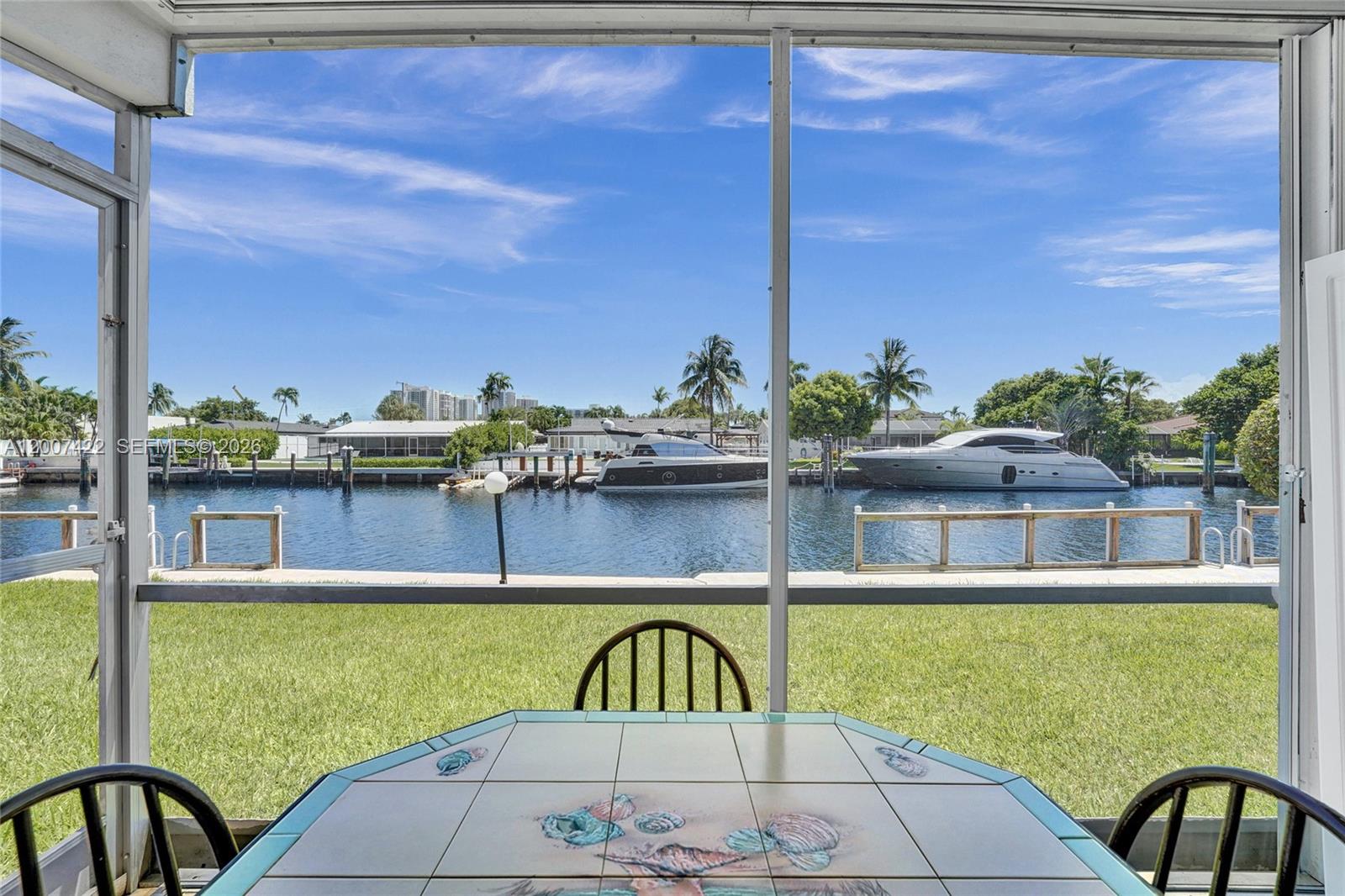A living room with tile floors and sliding glass doors opening to a waterfront patio — 455 Paradise Isle Blvd # 104, Hallandale Beach FL 33009, HALLANDALE BEACH, FL