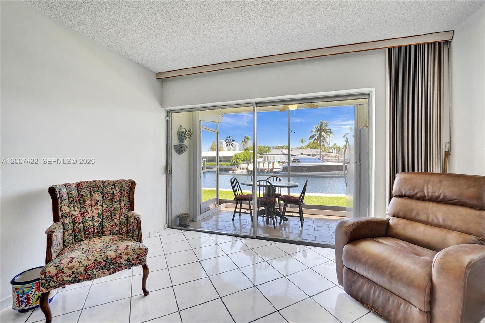 A living room with white tile floors, a beige sofa, and a sliding glass door — 455 Paradise Isle Blvd # 104, Hallandale Beach FL 33009, HALLANDALE BEACH, FL