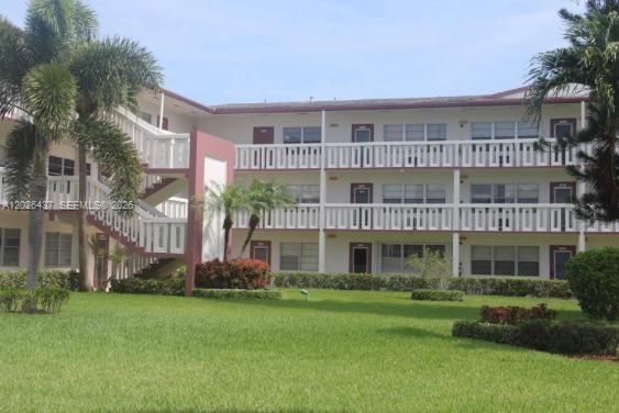 A three-story apartment building with white balconies and exterior staircases sits behind a grassy lawn — 449 Fanshaw K # 449, Boca Raton FL 33434, BOCA RATON, FL