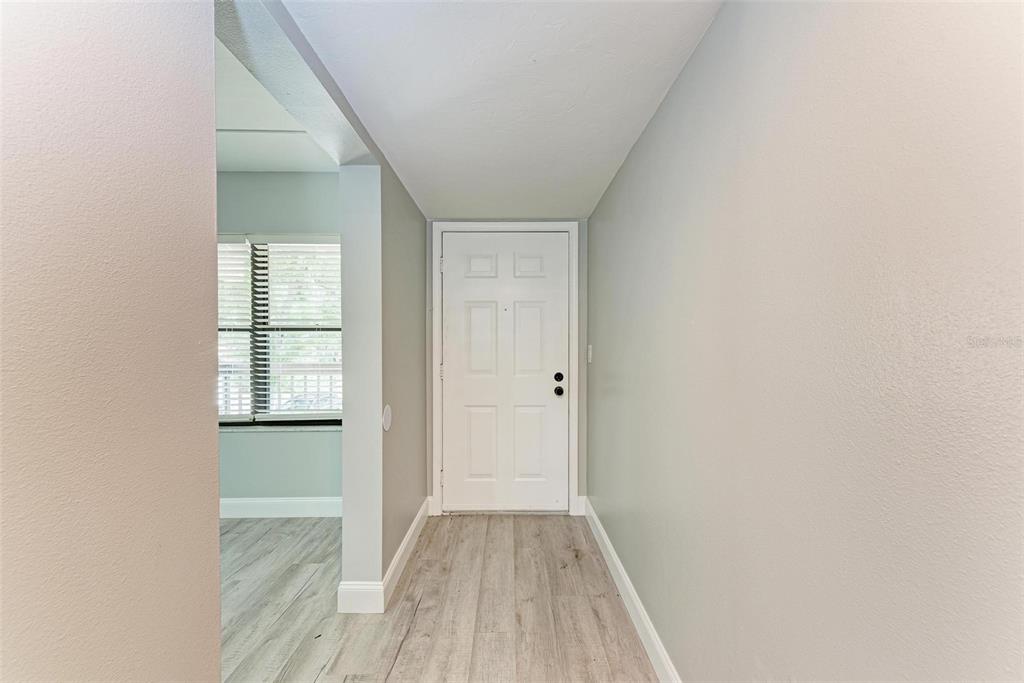 A white front door opens into a hallway with light wood-look flooring and gray walls — 515 30TH AVENUE W UNIT H201, BRADENTON, FL