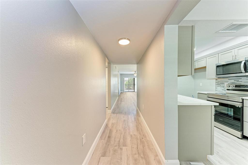 A hallway with light wood-look flooring leads toward a sliding glass door and kitchen — 515 30TH AVENUE W UNIT H201, BRADENTON, FL