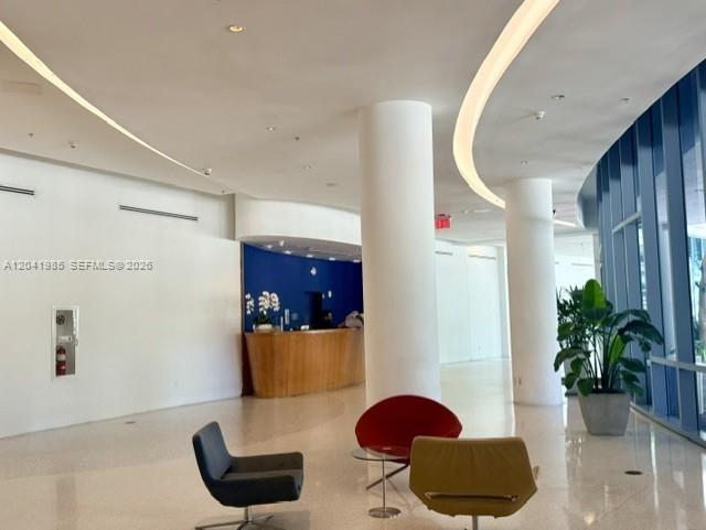 A modern building lobby features curved white walls, a wooden reception desk, and colorful chairs — 601 NE 36th St # 803, Miami FL 33137, MIAMI, FL